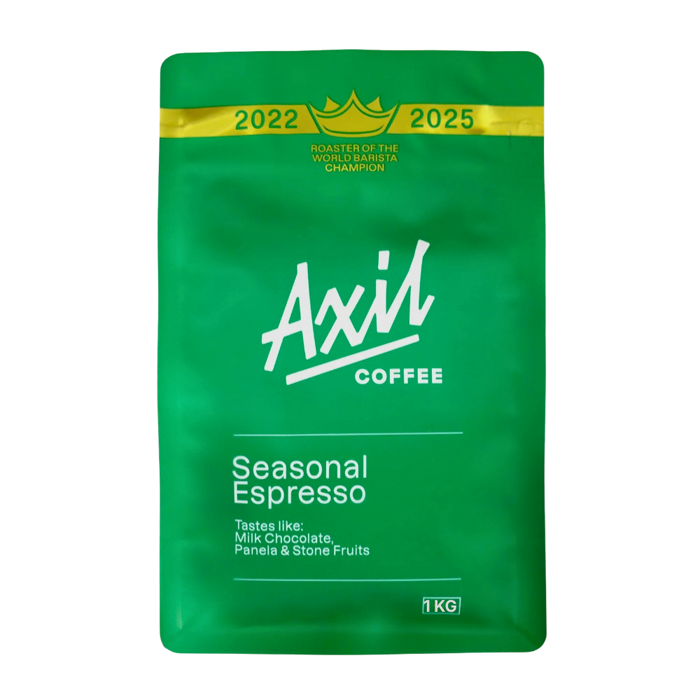 A 1kg green stand-up pouch of Axil Coffee Seasonal Espresso, featuring a gold band at the top with 2022 and 2025 roaster championship titles, and white branding text.