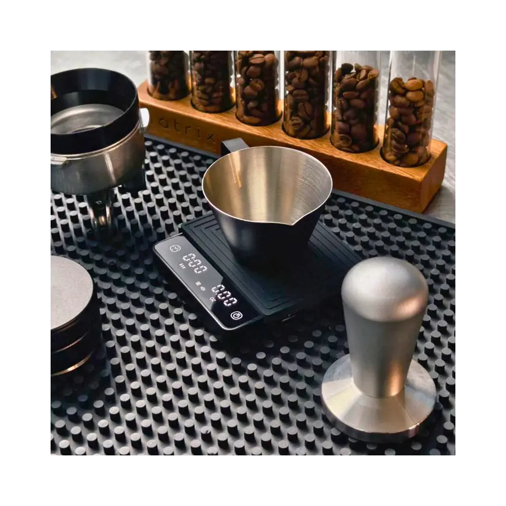 Coffee brewing equipment including a scale, funnel, and tamp on a textured surface with jars of coffee beans in the background.