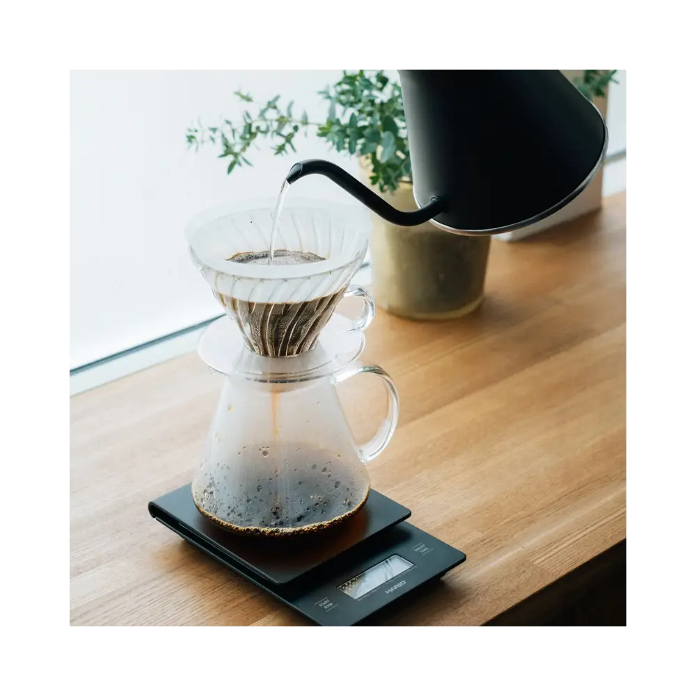 Coffee being poured into a glass carafe on a digital scale with a blurred background