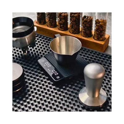Coffee brewing equipment including a scale, funnel, and tamp on a textured surface with jars of coffee beans in the background.