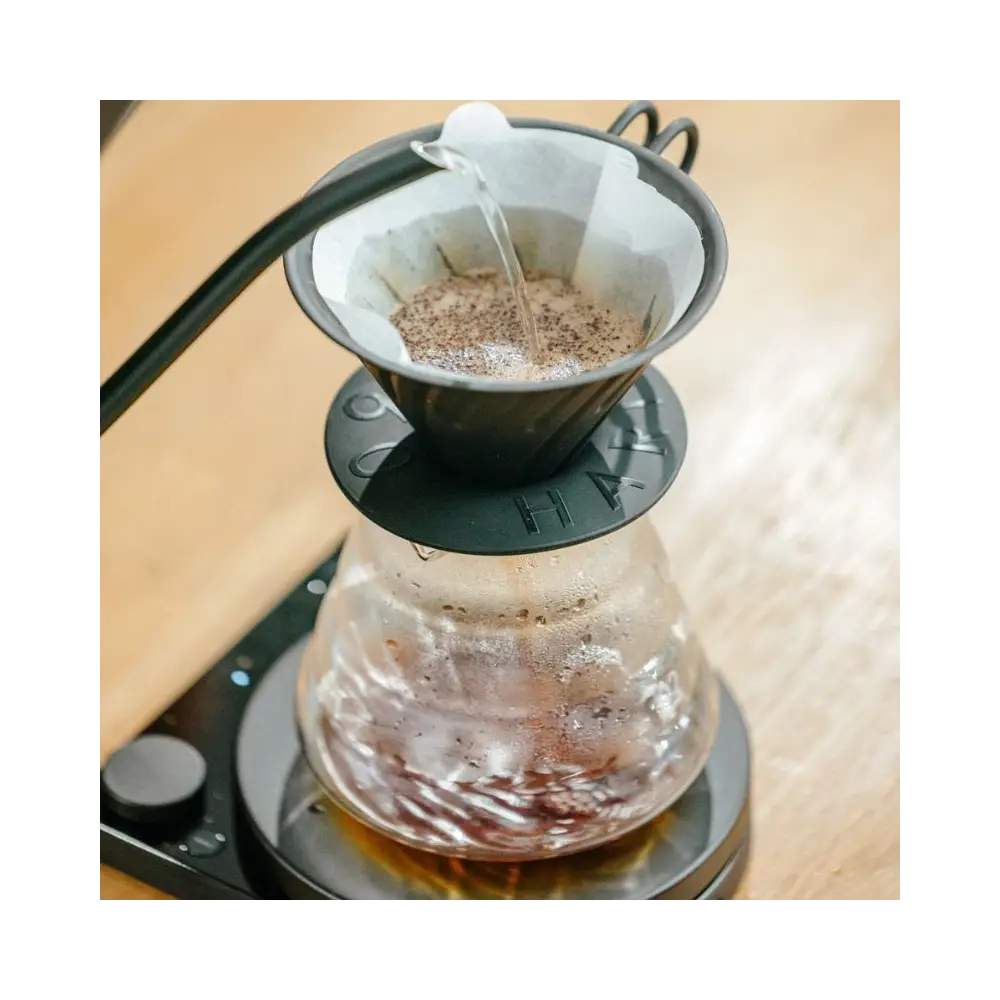 Coffee being poured into a glass carafe with a filter on a wooden surface.
