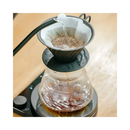 Coffee being poured into a glass carafe with a filter on a wooden surface.